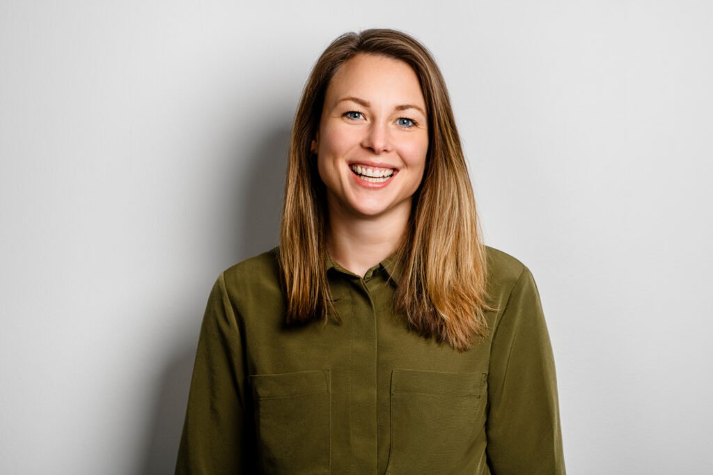 Lächelnde Frau in Olivgrüner Bluse vor neutralem Hintergrund für Business Portrait.