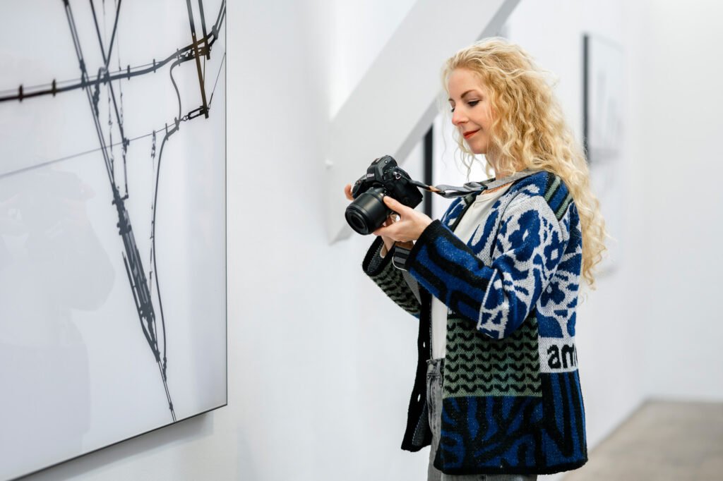 Fotografin mit Kamera bei der Arbeit in einer modernen Galerie, Fokus auf künstlerische Businessfotografie in Köln.