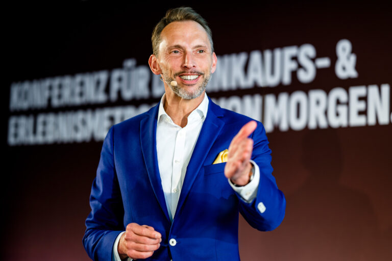 Mittelständischer Unternehmensberater in einem blauen Anzug hält einen Vortrag vor einem Publikum als Symbol für professionelle Beratung.